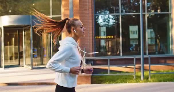 Sett fra siden av en sterk hvit kvinne i sportstrening, trening og løping. Ung idrettsutøver som driver med idrett for å holde seg i form på byens gate om morgenen. Helse, hardt arbeid. – stockvideo