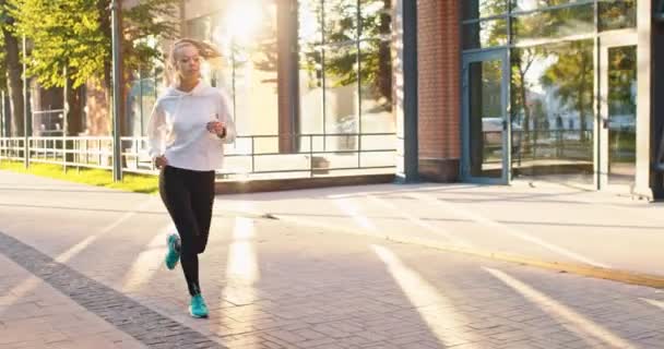 Sett fra siden av suksessfull jogging sportskvinne trene sengekonkurranse i urban gate. Ung hvit kvinnelig idrettsutøver som løper langs høye kontorbygg i byen. Helse, mesterskapskonsept. – stockvideo