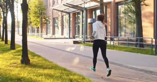 Bakifrån av atletisk kvinnlig sportwoman körs längs moderna kontorsbyggnader. Vuxen vit dam som idrottar, tränar, joggar på urban stadsgata. Friska och rika livsstil koncept. — Stockvideo