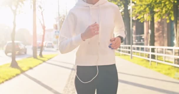 Front view of running Caucasian woman in sportswear working out to keep fit in morning. Adult female athlete in headphones listening to music and jogging in urban city street. Healthy lifestyle. — Stock Video