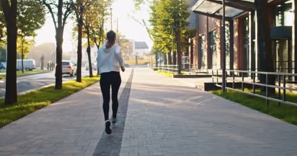 Back view of beautiful Caucasian sportswoman training and working out in morning. Young female athlete doing sports, running, jogging to lose weight in city street. Fitness, healthy lifestyle concept. — 图库视频影像