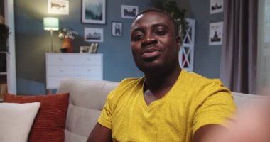 POV Charming 'li genç adam kanepede oturuyor ve evde video konferansı yapıyor. Afro-Amerikalı bir adam davet ediyor, izleyiciyi evine davet ediyor ve akşam vakti kameraya konuşuyor. İletişim konsepti.