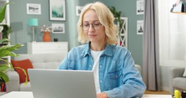 Neşeli, genç, beyaz gözlüklü, gözlüklü bir kadın bilgisayar başında çalışıyor, kameraya bakıyor ve gülümsüyor bilgisayar, iş, portre konsepti kullanarak oldukça mutlu bir kadın serbest yazar.