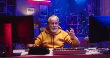 Kafkasyalı üst düzey erkek müzisyen kulaklıklı karışık konsol ve bilgisayar kullanarak ev stüdyosundaki masalarda renkli neon ışıkları eşliğinde müzik yaparken yaşlı DJ profesyonel ekipman üzerine yeni bir set hazırlıyor.