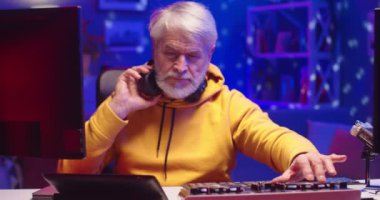 Kafkasyalı mutlu yaşlı DJ emeklinin portresini yakından çek. Profesyonel karıştırıcı konsolu ve bilgisayar üzerinde çalışıyor. Ev stüdyosunda dans müziği yaratıyor.