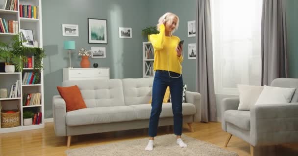 Szczęśliwa młoda biała ładna kobieta tańcząca w salonie w mieszkaniu słuchając muzyki w dobrym nastroju. Piękna radosna kobieta bawiąca się wykonując rytmiczne ruchy ciesząc się ulubioną piosenką — Wideo stockowe