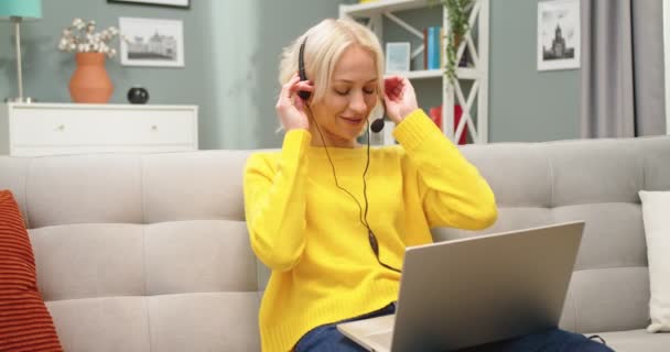 Portret van Kaukasische jonge mooie vrolijke vrouw videochatting in headset op video oproep op laptop online terwijl zittend op de bank in appartement, verre werk, videogesprek op de computer, freelance concept — Stockvideo