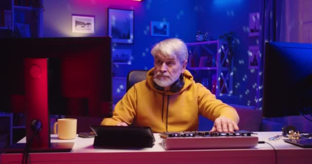 Portré régi férfi DJ működik a mixer konzol létrehozása zenét berendezések ül az asztalnál otthon gépelés számítógép streaming zene, modern professzionális DJ neon fények a házban — Stock videók