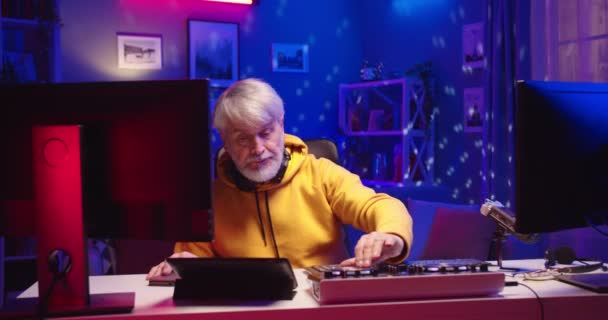 Blanc concentré vieil homme DJ professionnel travaillant dans le studio de disque à domicile utiliser surface contrôle table égaliseur mélangeur, néon coloré lumières, musicien senior streaming en direct sur ordinateur Concept de portrait — Video
