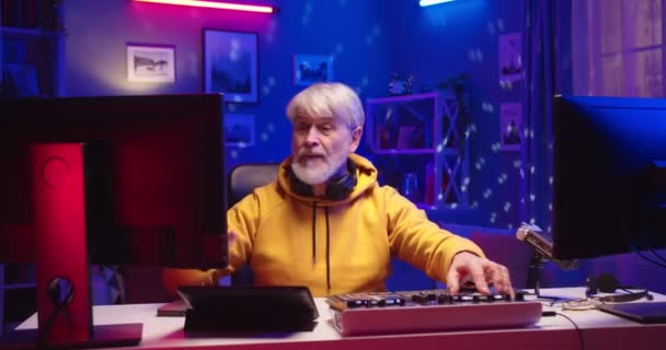 Portré régi kaukázusi vicces férfi profi DJ létrehozása tánc zene vezérlő asztal equalizer mixer dolgozik berendezések otthoni stúdió műhely neon fények jó hangulatban, zeneszerzés — Stock videók