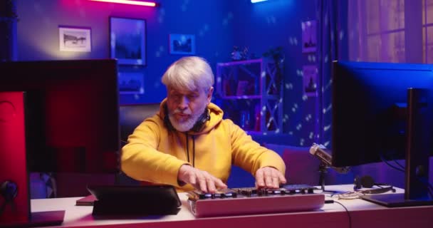 Portrait of Caucasian funny senior male professional DJ using control desk equalizer mixer working on dj set in home record studio in colorful neon lights, artist concept, musician art, dance music — Stock Video