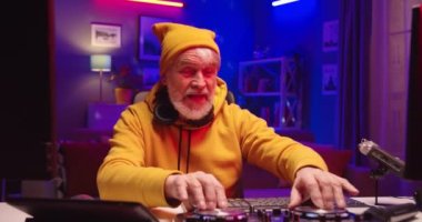 Kafkasyalı yakışıklı, neşeli, son sınıf öğrencisi DJ ev stüdyolarındaki masasında renkli neon ışıklarla müzik yaparken konsolu karıştırıp kameraya bakar ve gülümser, hobi konsepti oluşturur.