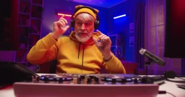 Tarz sahibi beyaz, neşeli, mutlu bir emeklinin evinde müzik dinleyip plaka akışı yapan eski erkek DJ 'in konsol mikseri üzerinde çalışırken neon ışıklı bir odada oturması.