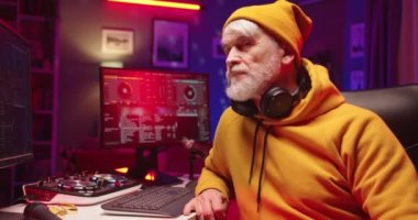 Şık, emekli, yakışıklı, beyaz erkek dj 'nin yakın çekimde çekilmiş bir portresi. Kameraya bakıyor ve akşamları müzik dinleyerek ev kayıt stüdyosunda şarkı dinliyor. Konsol karıştırılıyor Bilgisayarda müzik oluşturuluyor