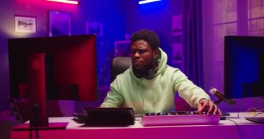Yakışıklı Afro-Amerikalı genç DJ 'in portresi Neon ışıklı stüdyoda oturmuş profesyonel mikser konsolu üzerinde çalışıyor bilgisayar monitörlerine bakıyor, şarkı besteleyen müzisyen