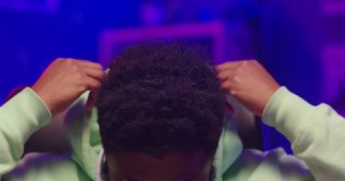 Mutlu Afro-Amerikalı genç yakışıklı DJ 'in karanlık odada oturup, neon ışıkta ev stüdyosunu kaydedip, kameraya iyi haliyle bakıp göz kırpmasına yakın durun. Evde erkek DJ beste yapıyor.