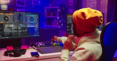 Kapatın. Pozitif Afrika kökenli genç erkek ses mühendisi sarı şapkalı, mikser konsolu üzerinde çalışıyor bilgisayar ekranına bakıyor ses ritmlerini karıştırıyor, DJ 'lik yapıyor.