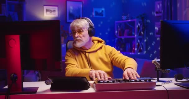Portret starego, białego, brodatego emeryta transmitującego na żywo DJ-a w domu pracującego nad profesjonalnym sprzętem konsoli mikserskiej podczas blokady koronawirusów, strumieniowego podcastu — Wideo stockowe