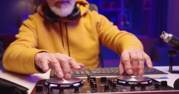 Közeli kép hűvös elegáns fehér szakállas idősebb férfi DJ ül íróasztal sötét szobában neon fények dolgozik konzol mixer berendezések keverés új tánczene, hangverés készítő — Stock videók