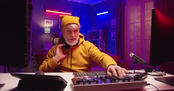 Vit vacker glad glad glad senior manlig DJ musiker i hörlurar med hjälp av att blanda konsol och teknik samtidigt skapa musik vid skrivbordet i hemstudio med färgglada neon ljus, hobby koncept — Stockvideo