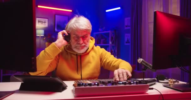 Close up of handsome Caucasian funny modern happy old man mixing on vinyl plate streaming live playing music at home recording studio. Male DJ creating electronic music on console mixer streaming live — Stock Video