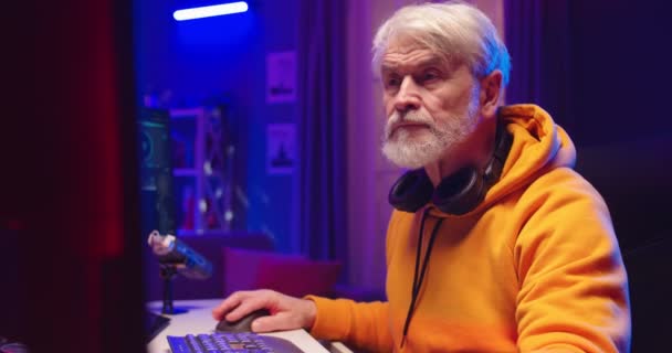 忙しい白人スタイリッシュな老人DJのクローズアップは、新しいシングルを録音ホームスタジオでライブ演奏をストリーミングビニールプレート上で混合します。男性DJは、コンピュータ上のコンソールミキサーで電子音楽を作成します — ストック動画