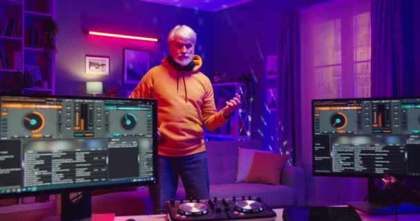 Senior Kaukasische bebaarde man in stijl staande in donkere woonkamer doen alsof ze gitaar spelen in huis opnamestudio met mengbord en computer monitoren, mixer console, oude Dj concept — Stockvideo