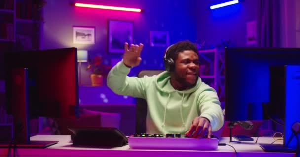 Portret van vrolijke positieve jongeman DJ speelt muziek op mixboard en vinyl plaat thuis opnamestudio in neon licht. Happy African American guy creëren beat op mixer console muzikant concept — Stockvideo