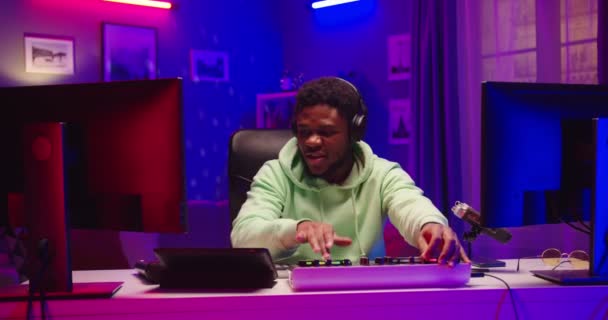 Portré vicces pozitív fiatal afro-amerikai férfi DJ zenét játszik keverő fórumon és vinil lemez otthon stúdió neon fény utánozza gitározás és mosolygós élvezi a munkafolyamatot — Stock videók
