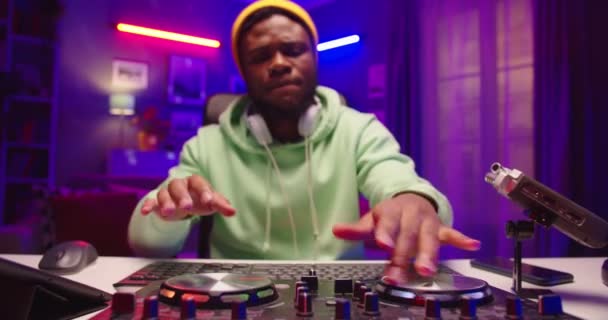 Afrikai amerikai fiatal profi férfi DJ klubzenét játszik lemezjátszó konzolon otthoni stúdióban neon fényben. Közeli kép jóképű kreatív férfi kaparja vinyl esztergáló karok keverő — Stock videók