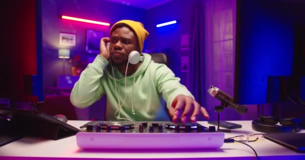 Primer plano del alegre hombre emocional afroamericano dj creando música de club en la consola giratoria sentado en el estudio de grabación en casa rascando vinilo tocando y transmitiendo música en vivo, concepto de músico — Vídeo de stock