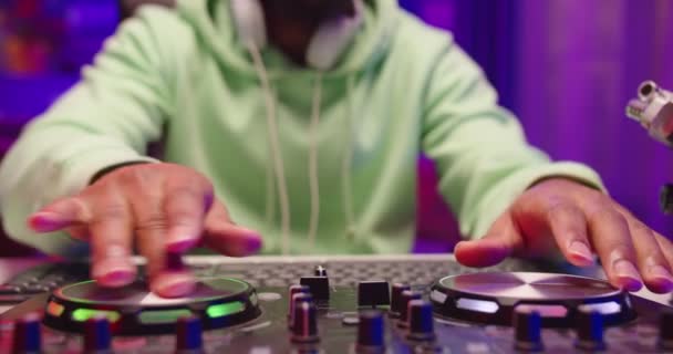 Close up shot of African American male DJ hands playing music on turntable console in home recording studio. Man fingers scratching vinil and turning levers on mixer controller, sound beat concept — Vídeo de Stock