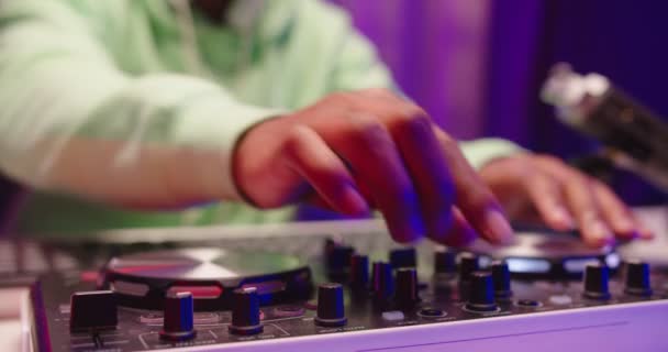 Primer plano de chico afroamericano manos tocando música del club en la consola del mezclador en el taller de estudio de grabación en casa. Hombre dedos rascando vinilo y girando palancas en controlador de mezcla, concepto dj — Vídeo de stock