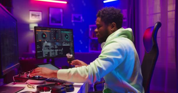 Side view of young African American handsome male dj sitting at table mixing music performing streaming live from home recording studio working on mixer console using computer, audio engineer concept — Stock Video