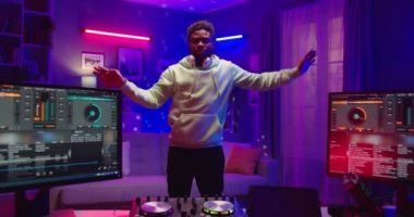 Afro-Amerikalı genç neşeli erkek, karanlık odada neon ışıklarıyla stüdyoda dans ediyor ve eğlenceli hareketler yapıyor. Keyfi yerinde, DJ konsepti.