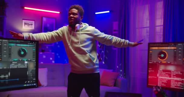 African American νεαρός χαρούμενος όμορφος dj στέκεται στο διαμέρισμα στο νέον φως στο σπίτι ηχογράφηση στούντιο χορό και ρυθμικά κινείται ακούγοντας μουσική κλαμπ διασκεδάζοντας, αναψυχή, χορό — Αρχείο Βίντεο