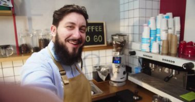 Kafe işyerinden canlı yayın yapan beyaz erkek blogcu POV 'u. Genç erkek barista, kahve dükkanında takipçilere, izleyicilere konuşuyor ve kamerada konuşuyor. İş, sosyal medya kavramı.