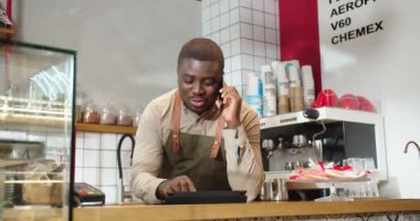 Modern kahve dükkanında çalışan yakışıklı bir erkek, telefonla konuşuyor. Genç baristanın müşteri, müşteri siparişini alıp tablete koyması. İş, restoran konsepti.