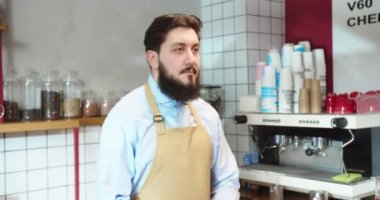 Kahve dükkanında çalışan ve barın arkasında duran yakışıklı adamın portresi. Erkek barista kameraya bakıyor ve kafede kollarını kavuşturuyor. İş, hizmet, meslek, girişimci kavramı.