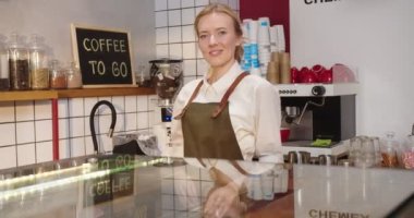 Önlük giyen, kahve dükkanında çalışan güzel beyaz bir kadın. Barın arkasında durup kameraya bakıp gülümseyen genç bir kafe sahibinin portresi. İş, girişimcilik kavramı.
