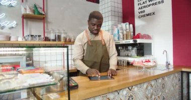 Kafede çalışan Afro-Amerikalı bir barista, işyerindeki tablette yazıyor. Genç bir erkek çalışan hisse senedi ve muhasebe masraflarını kontrol ediyor. Küçük işletmelerin masrafları. Finans, hizmet kavramı.
