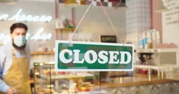 Happy male cafe manager flipping CLOSED to OPEN sign on window in coffee shop. Young Caucasian man smiling looking outside and waiting for customers. Small business, people and start-up concept. — Stock Video