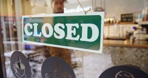 Outdoor uitzicht van de mannelijke cafe eigenaar flippen Gesloten te OPEN teken op venster in coffeeshop. Jonge blanke man die zaken begint en op klanten wacht. Het concept "kleine ondernemingen, mensen en startende ondernemingen". — Stockvideo