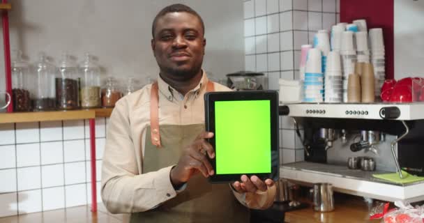 커피숍에 녹색 화면 이 있는 디지탈 태블릿을 들고 있는 매력적 인 남성 바리스타. 아 프로 미국인 성인 남성, 가젯에 크로마 키를 표시합니다. 작은 사업, 기업가 정신. — 비디오