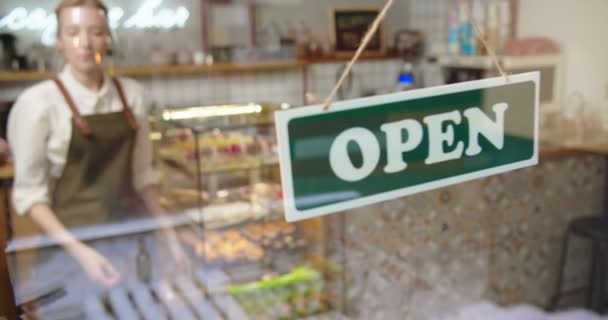 Üzgün kadın kafe sahibi Coronavirus yüzünden kafeyi kapatıyor. Kafkasyalı genç barmen, maske takıyor. Üzgünüm. Pencereye kapalı duyuru ve açık işareti yapıyoruz.. — Stok video