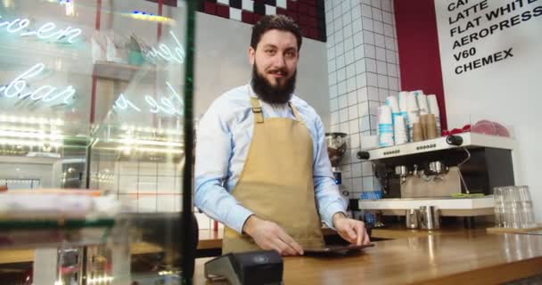 Retrato de barista masculino guapo trabajando y parado detrás de la barra en la cafetería urbana. Hombre caucásico adulto barista usando tableta digital, tomando pedidos y mirando a la cámara. Concepto empresarial. — Vídeos de Stock