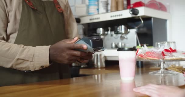 Közelkép afro-amerikai barista tartja terminál a női vásárlók. Az ifjú hölgy fizeti a rendelést és kávét iszik a kávézóban. Érintésmentes fizetés, NFC technológia koncepció. — Stock videók