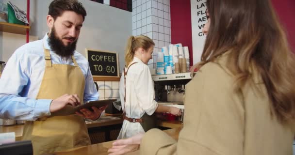 Professionele mannelijke barman neemt de bestelling van de klant en zet het eigen op tablet. Jonge vrouwelijke werknemer die koffiebeker naar mooie dame houdt en glimlacht. Service, bedrijfsconcept. — Stockvideo