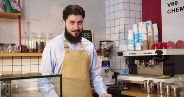 Atrakcyjny właściciel kawiarni stoi za barem i pokazuje znak OPEN. Dorosły biały mężczyzna w fartuchu, patrzący w kamerę i uśmiechający się. Kwarantanna, biznes, koncepcja kariery. — Wideo stockowe
