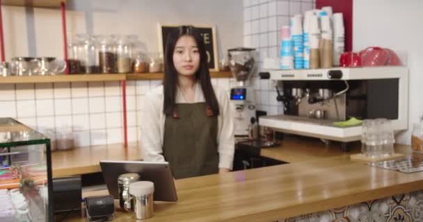 Snygg kvinnlig barista som står bakom baren i caféet. Ung dam kvinna tittar på kameran, snärja och korsa armar. Småföretag, arbete, yrkesbegrepp. — Stockvideo